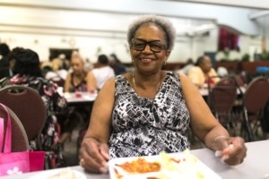 A woman in a black and white sleeveless shirt enjoys a meal at the Greater Galilee Baptist Church. 