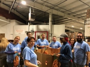 A group of eight volunteers wearing American family Insurance blue shirts and standing around a big box of carrots. 