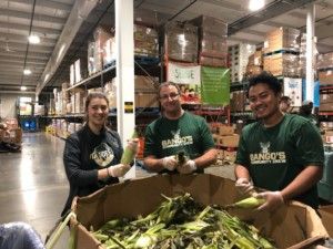 A group of three volunteers wearing green Bucks shirts in front of a big box of corn. 