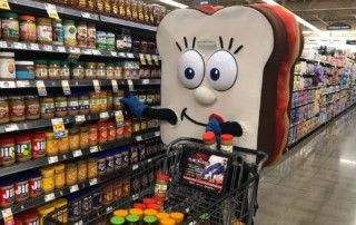 A peanut butter and jelly mascot with a silly smile stocking a cart of peanut butter and jelly.
