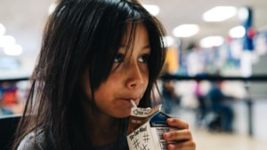 Young girl with straight dark hair drinking a carton of chocolate milk. Children who are eligible for free or reduced-price school meals through the National School Lunch Program may be eligible for EBT. 