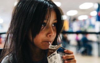 Young girl with straight dark hair drinking a carton of chocolate milk. Children who are eligible for free or reduced-price school meals through the National School Lunch Program may be eligible for EBT.