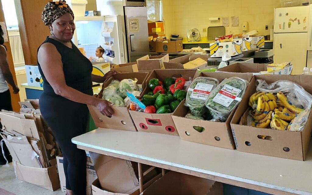A woman stands next to boxes of fresh produce at a food pantry