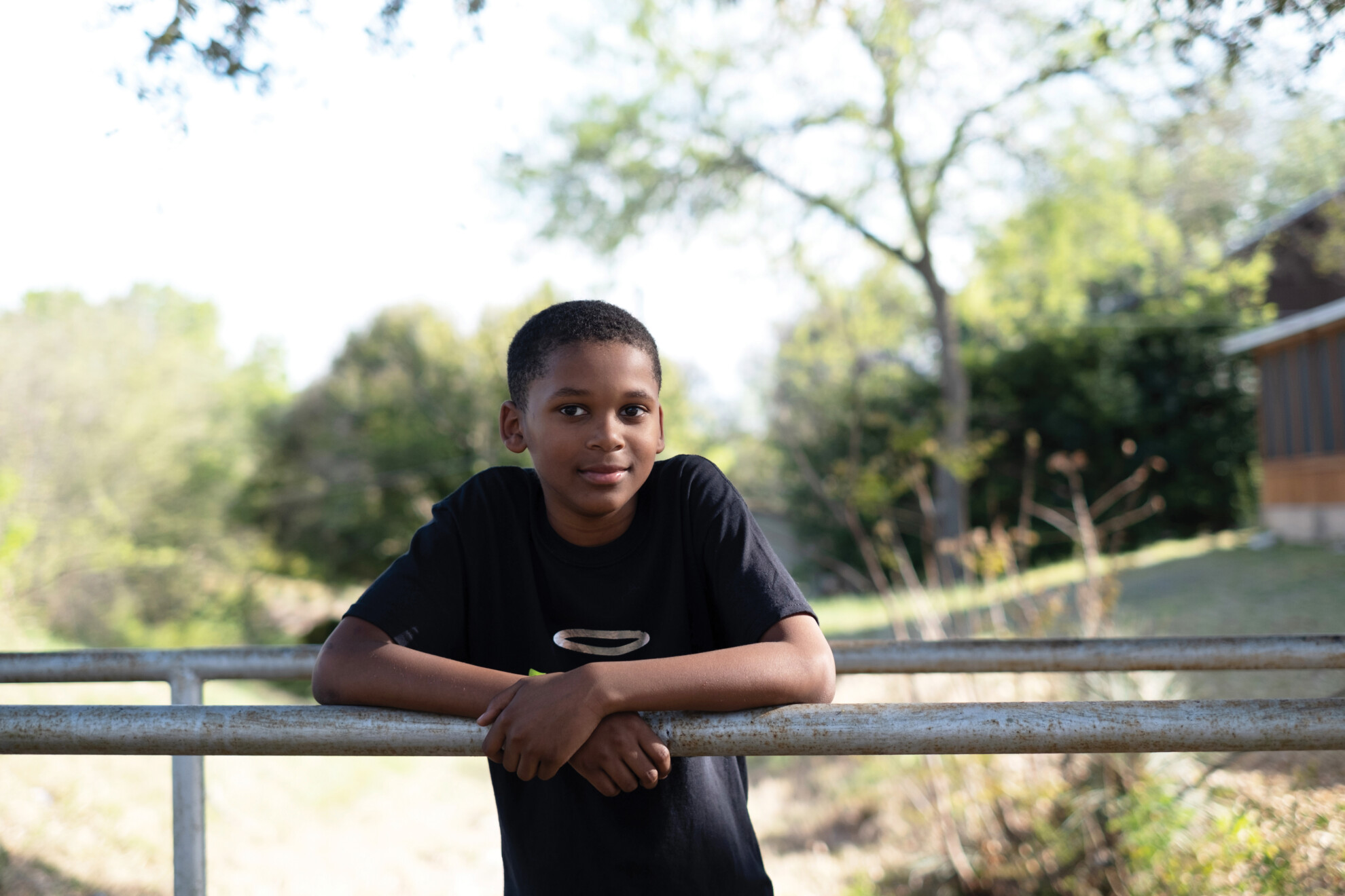 A young boy wearing a black t-shirt, Elijah, leans against a fence.